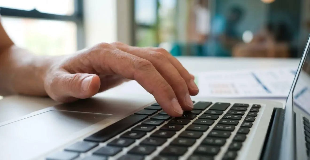 Gros plan sur des mains tapant sur le clavier d'un ordinateur portable moderne, avec un document financier flouté en arrière-plan